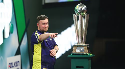 Luke Littler zeigt auf den Weltmeister-Pokal